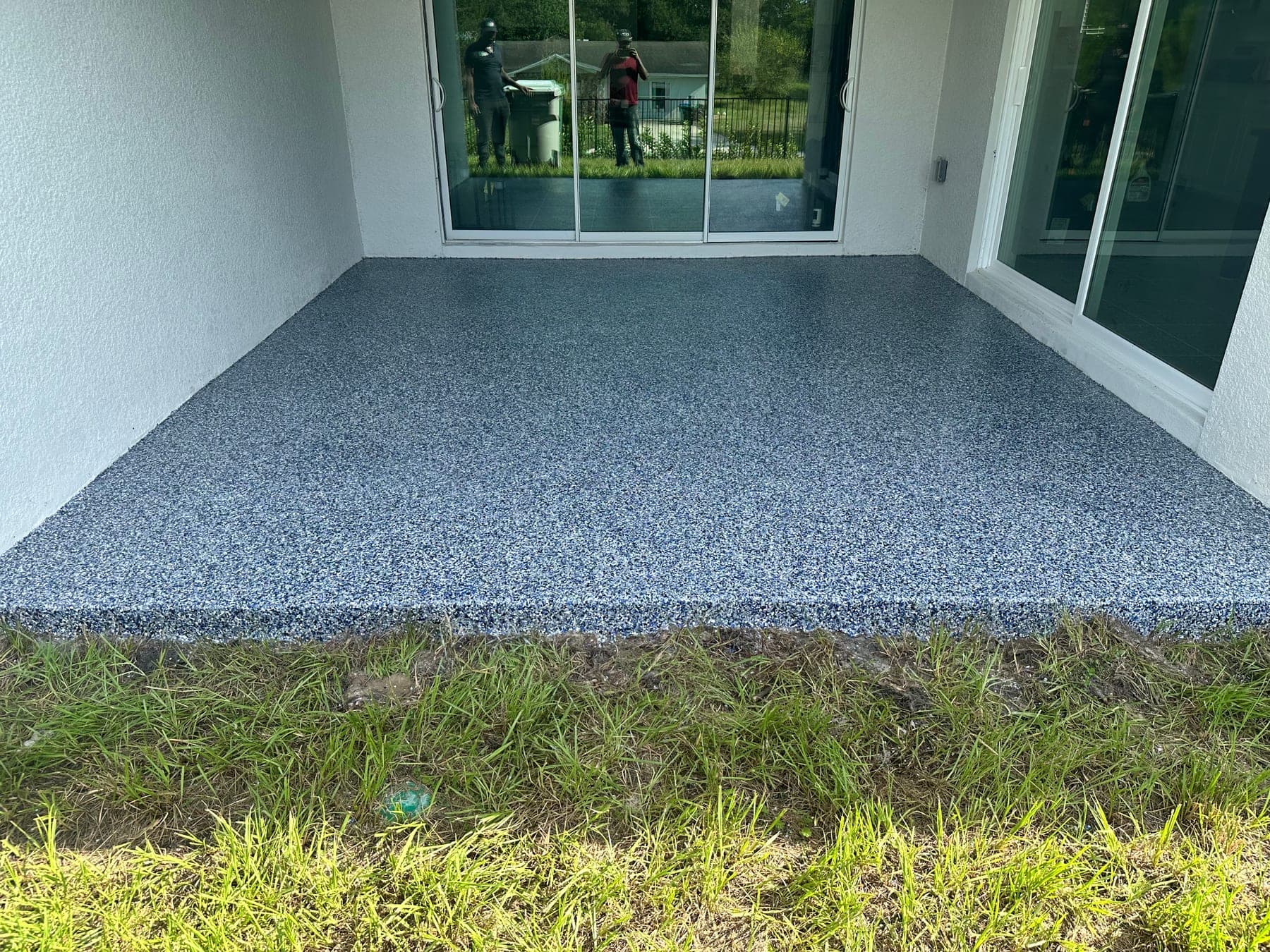 Covered back patio finished in blue and grey flake epoxy, beside sliding glass doors and a lawn.