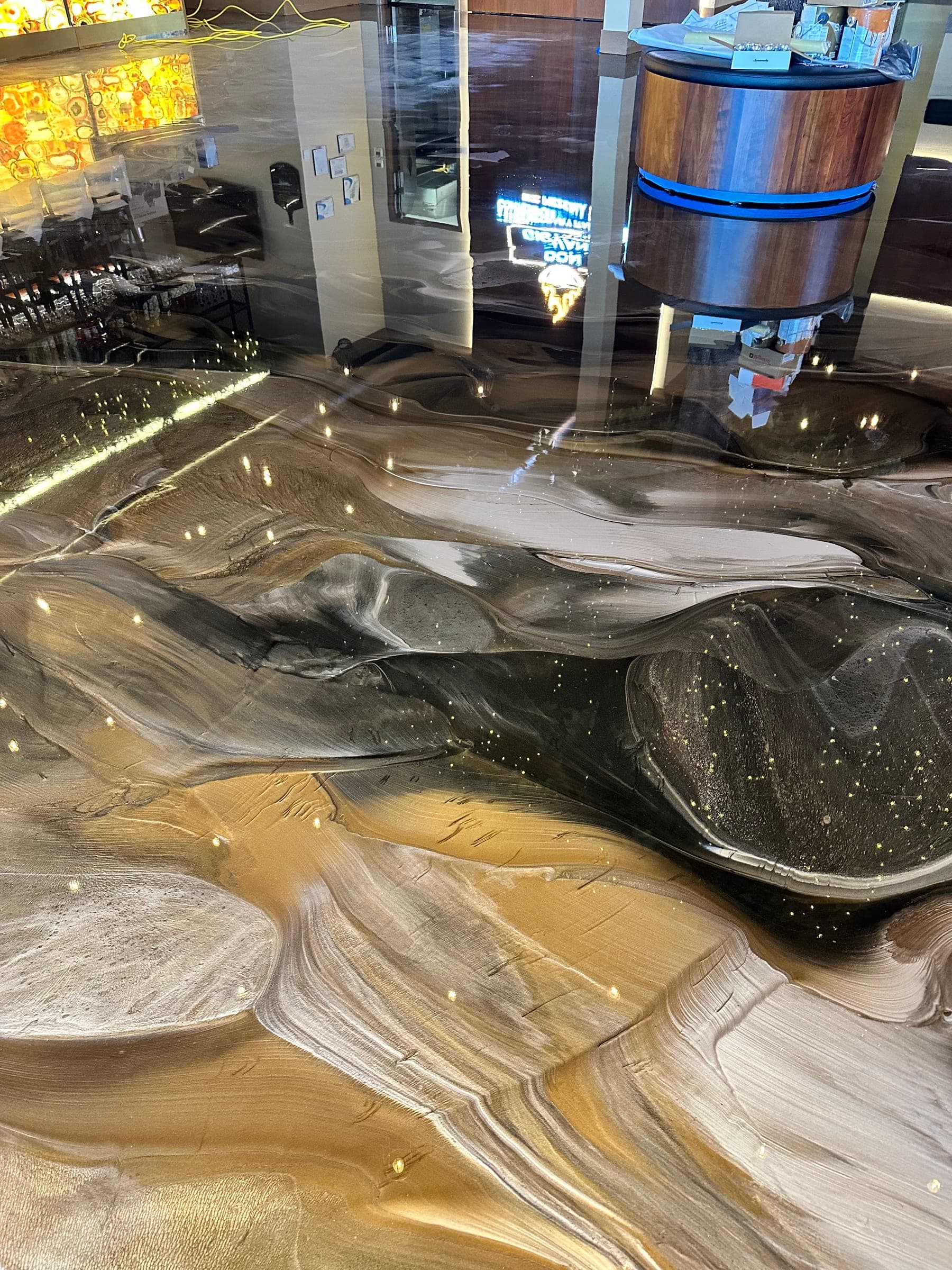 Close-up of a black, gold and cream marbled metallic epoxy floor with small specks of light, in a commercial lobby.