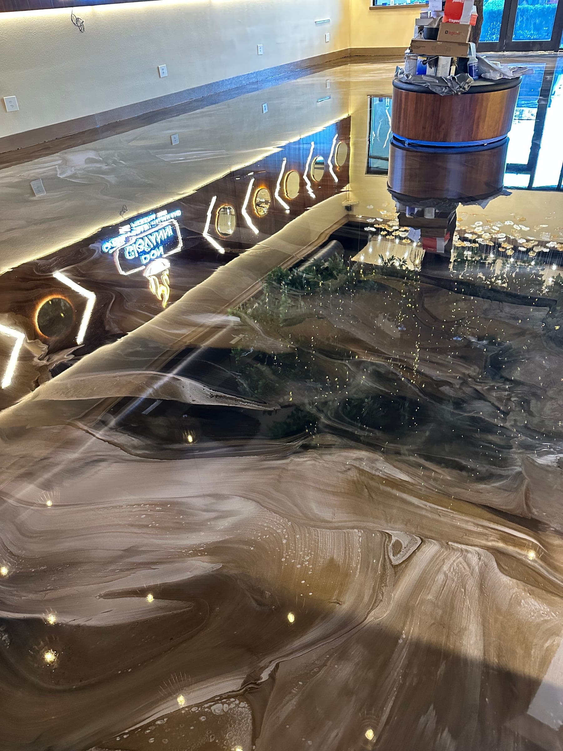 Glossy brown and cream metallic epoxy floor in a commercial lobby, reflecting the wall lighting and a round wood-panelled counter.