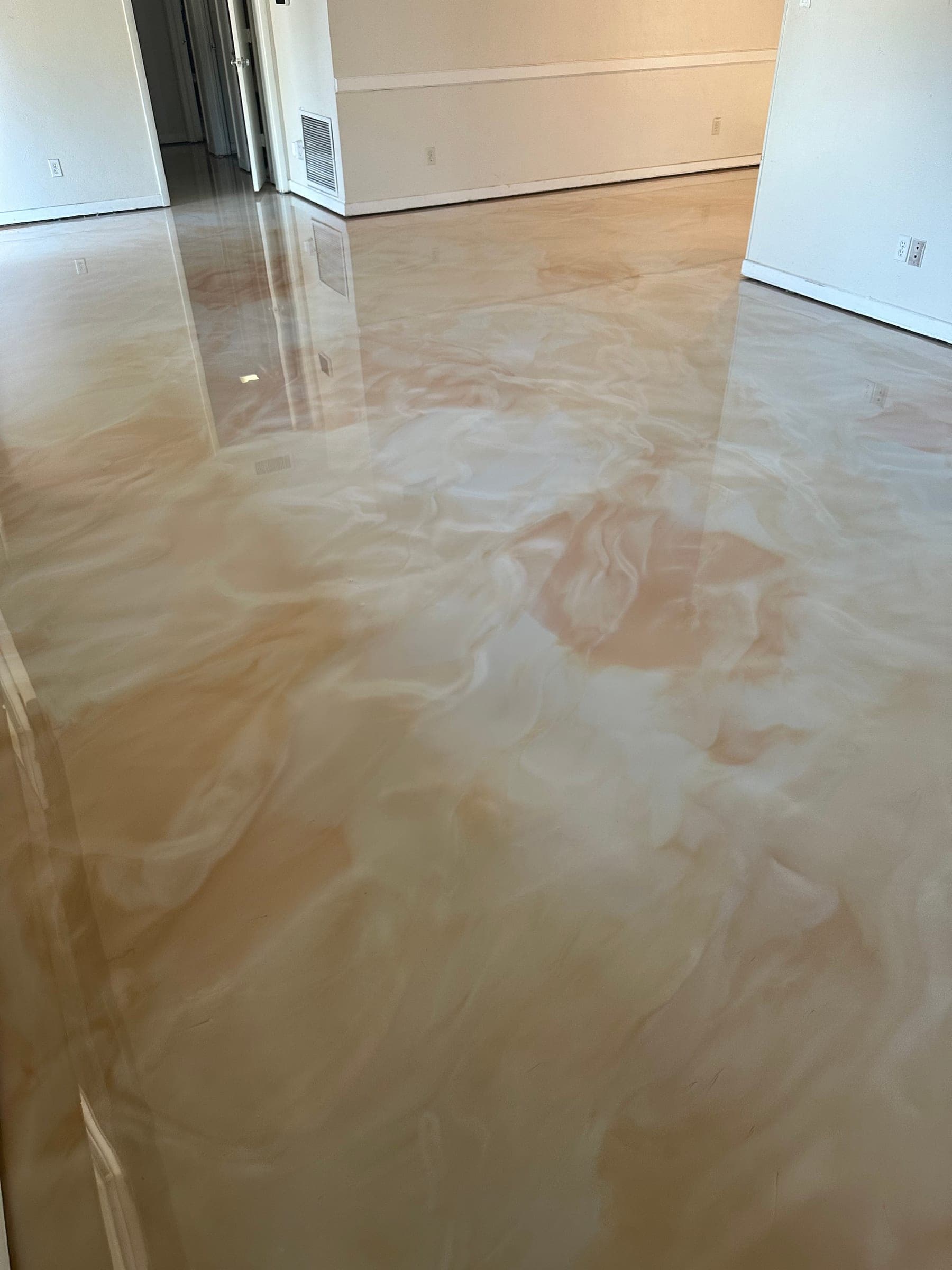 Glossy cream and peach swirled metallic epoxy floor across an empty living area in a home.