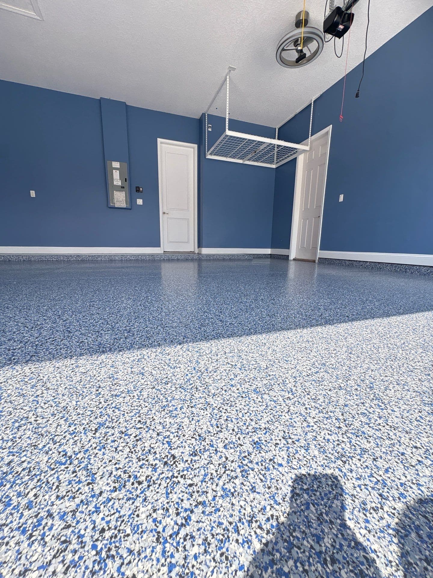 Blue, grey and white flake garage floor beneath blue walls and an overhead storage rack.