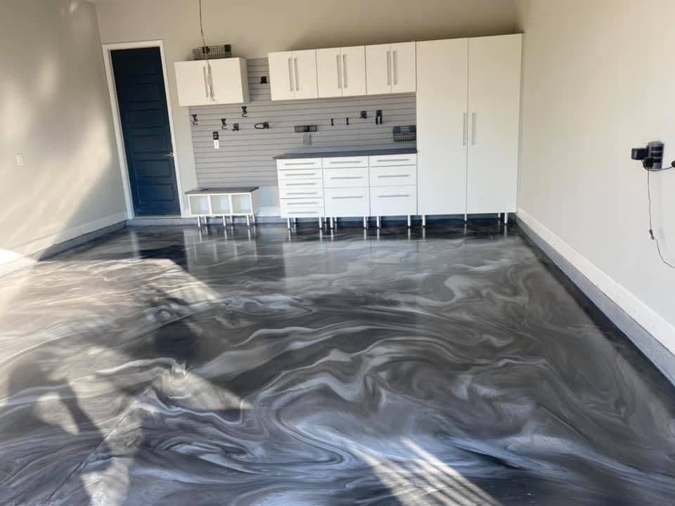 Glossy grey, black and silver swirled metallic garage floor in front of white storage cabinets.