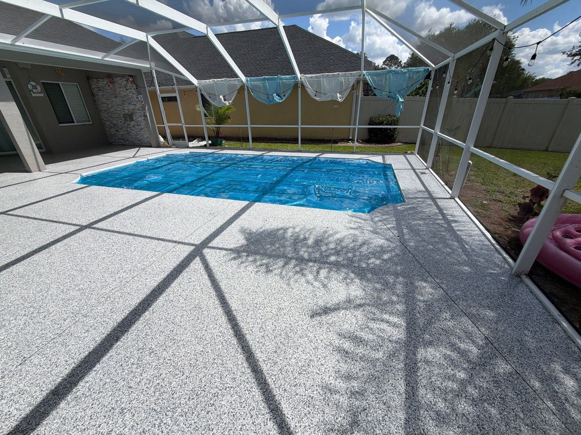 Grey speckled pool deck around a blue swimming pool inside a screened enclosure.