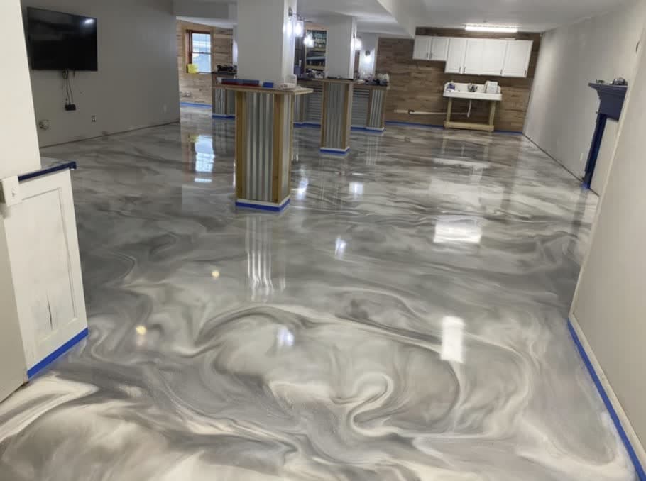 Grey and white marbled metallic epoxy floor, freshly poured and still taped at the baseboards, in an open-plan basement bar.